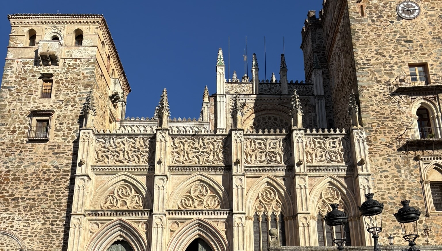 The monastery of Guadalupe with its imposing stone towers and gothic architecture, set against a hillside. The historic religious complex dominates the town with its fortress-like appearance.