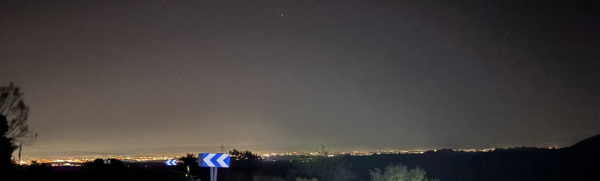 A panoramic night view of Madrid from a high vantage point, with city lights illuminating the urban landscape under a dark sky.