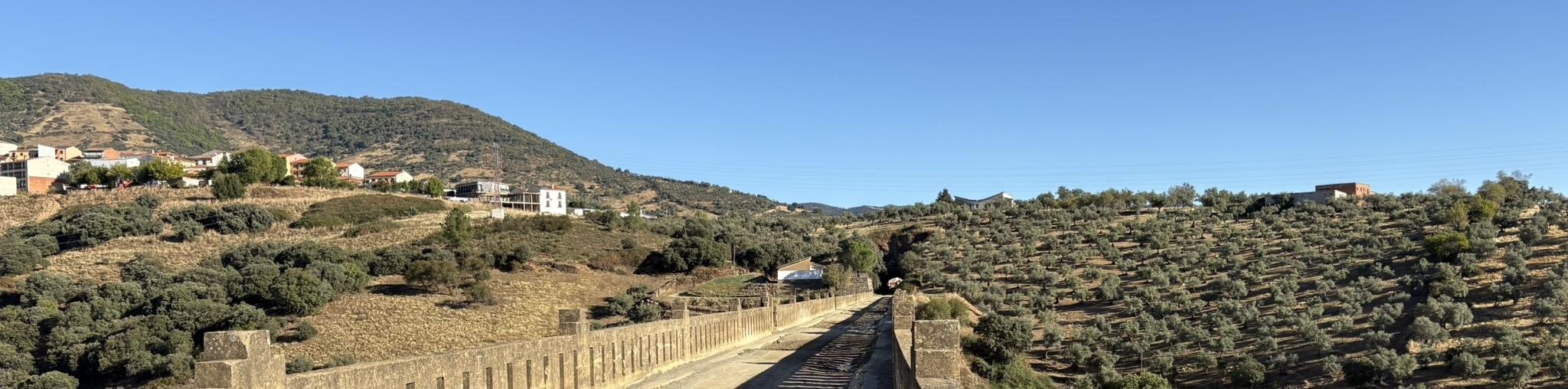 A historic stone viaduct with multiple arches spanning across a deep gorge, surrounded by steep rocky cliffs and vegetation. The old train line structure is impressive against the rugged landscape.