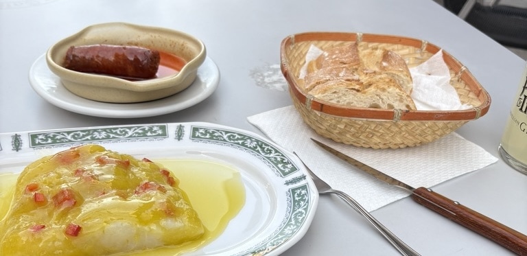 A plate with warm chorizo sausage and marinated raw cod topped with olive oil and paprika, served on a white plate in a Spanish bar.