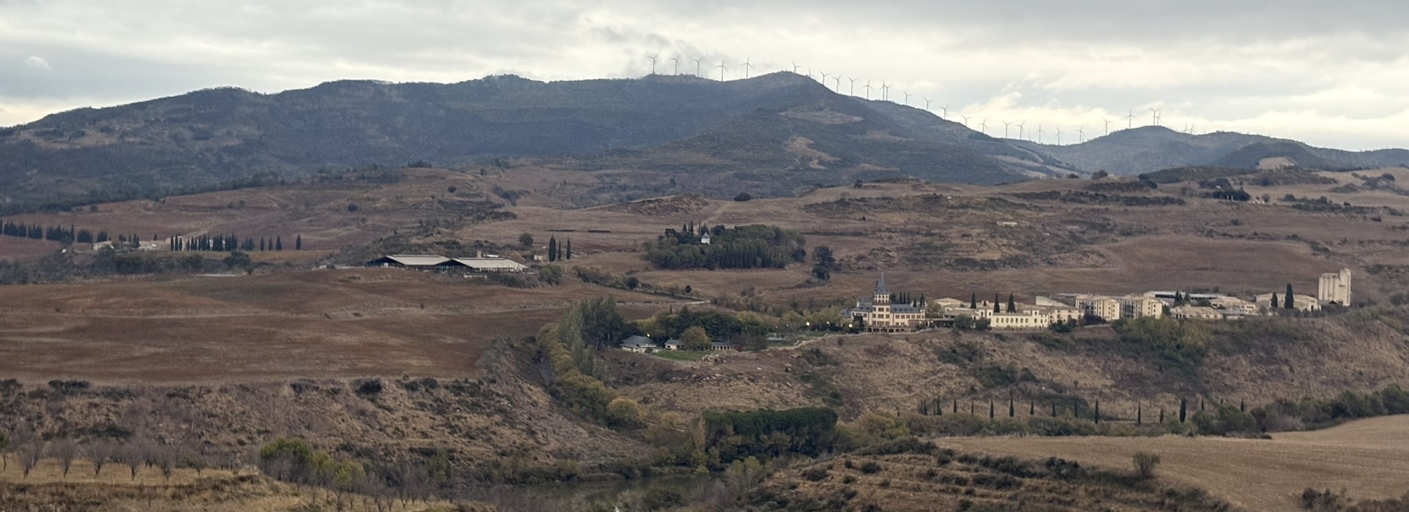 A village in the dry mountains surrounded by hills topped with wind turbines