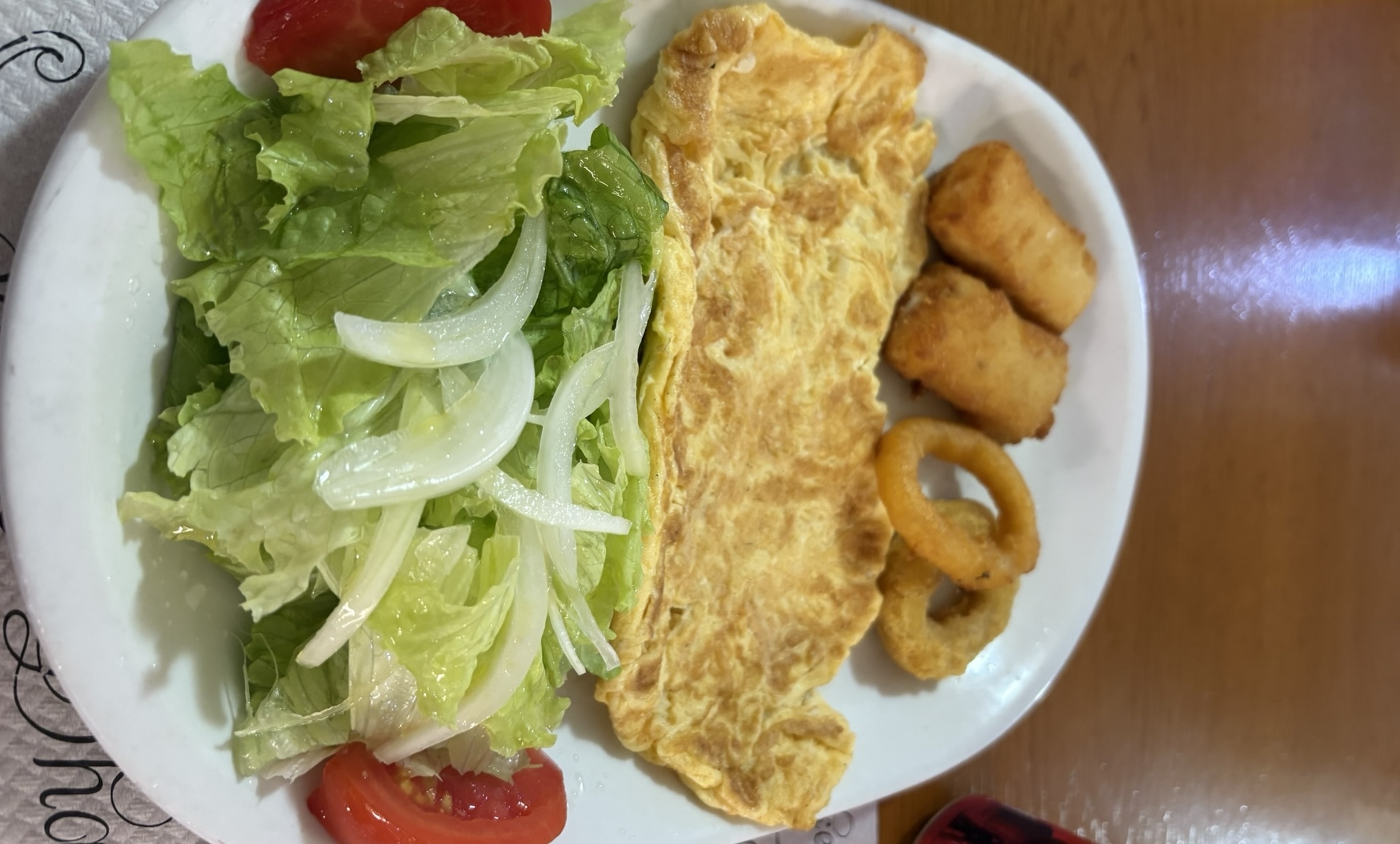 A simple Spanish dinner spread featuring tortilla, fresh salad, croquetas, and a cheese sandwich on white plates, served at a hostal dining table.