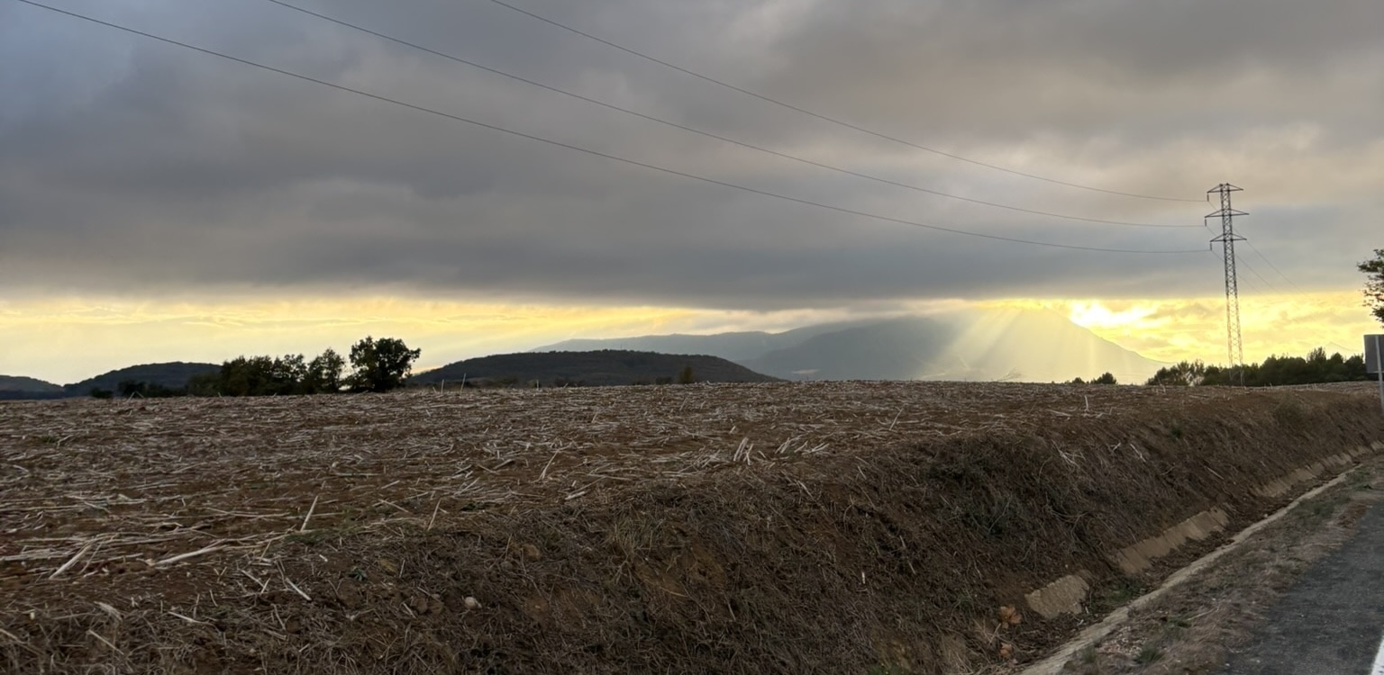Sunset going through the clouds along an empty field with mountains in the background.