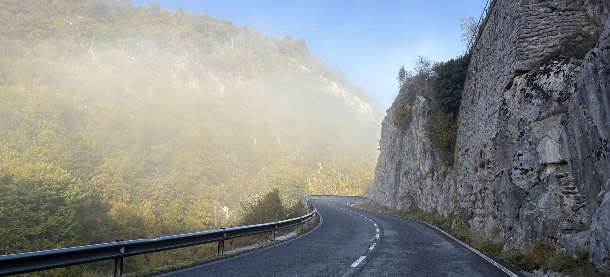 View from a hill over a valley with fog covering the lower parts. Some trees and hills are poking through the fog.