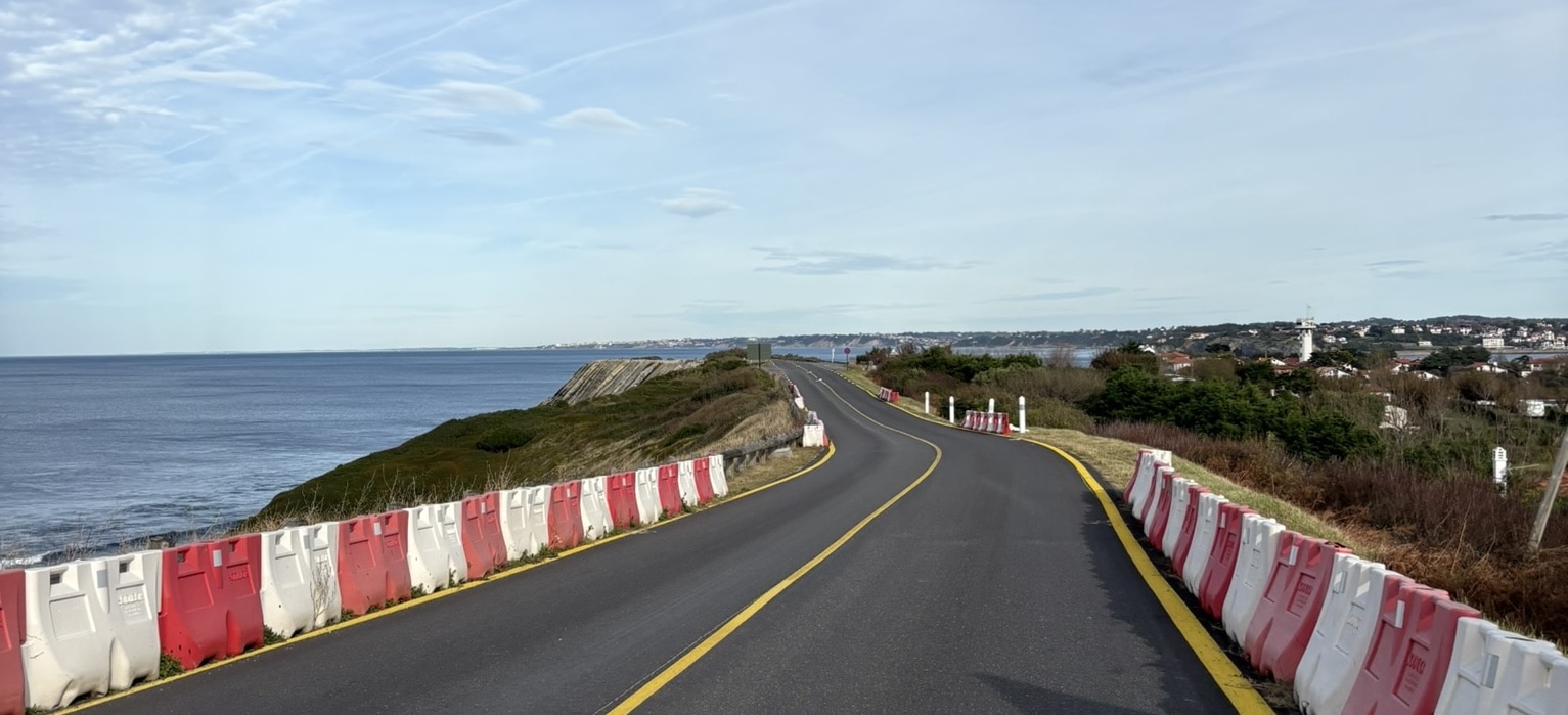 A newly resurfaced road with orange markings. Bright sky overlooking the sea, the green country side and Saint-Jean-de-Luz